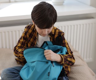 Photo of Boy packing backpack for school on bed at home