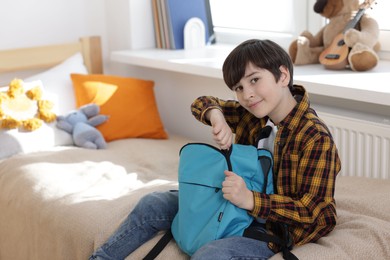 Boy packing backpack for school on bed at home, space for text