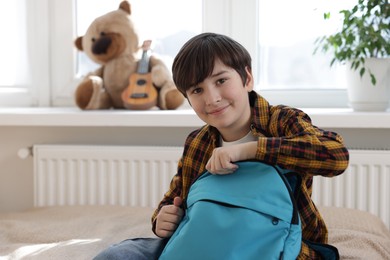 Photo of Boy packing backpack for school on bed at home, space for text