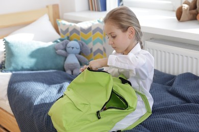 Photo of Girl packing backpack for school on bed at home