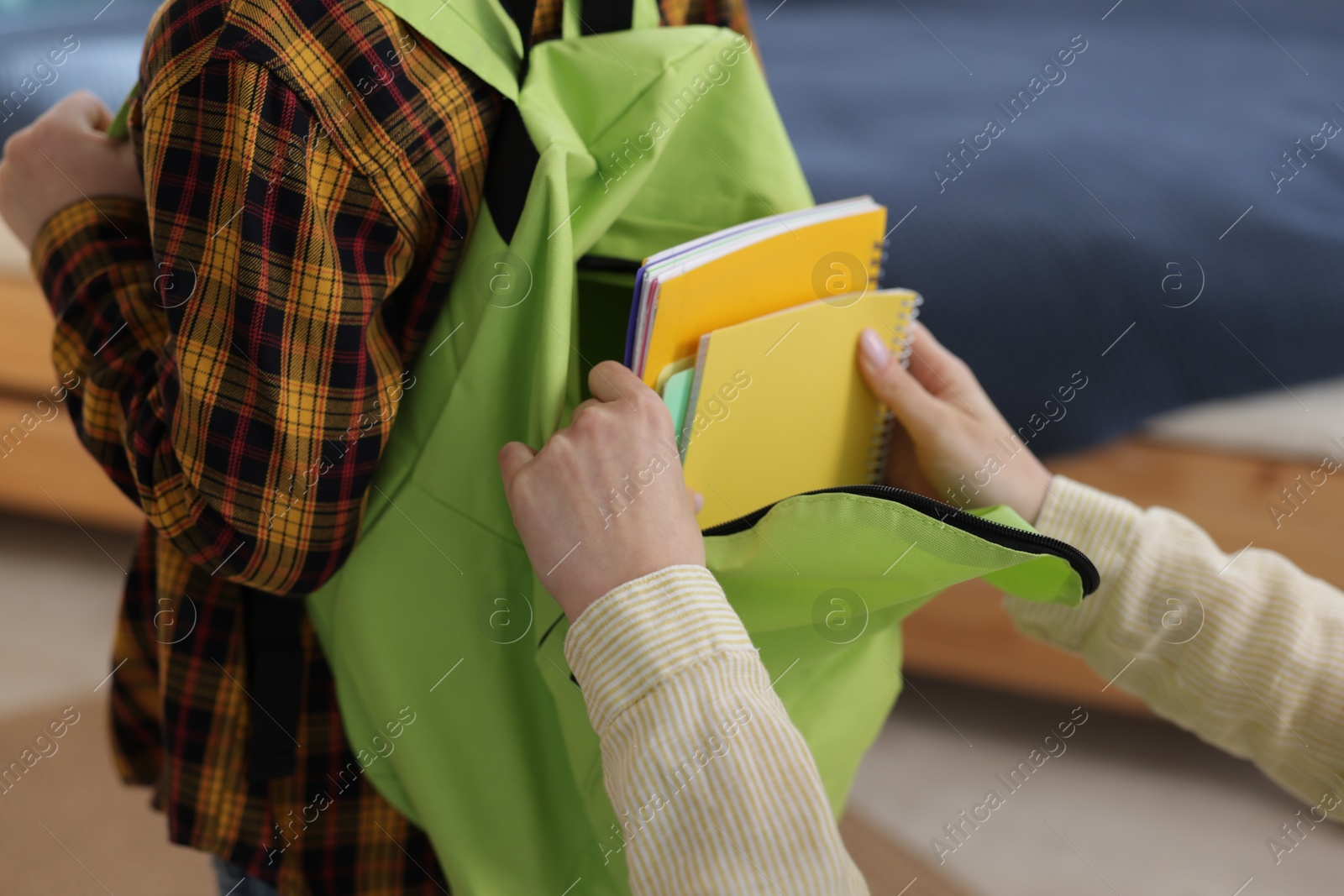 Photo of Mother helping her son packing backpack for school at home, closeup