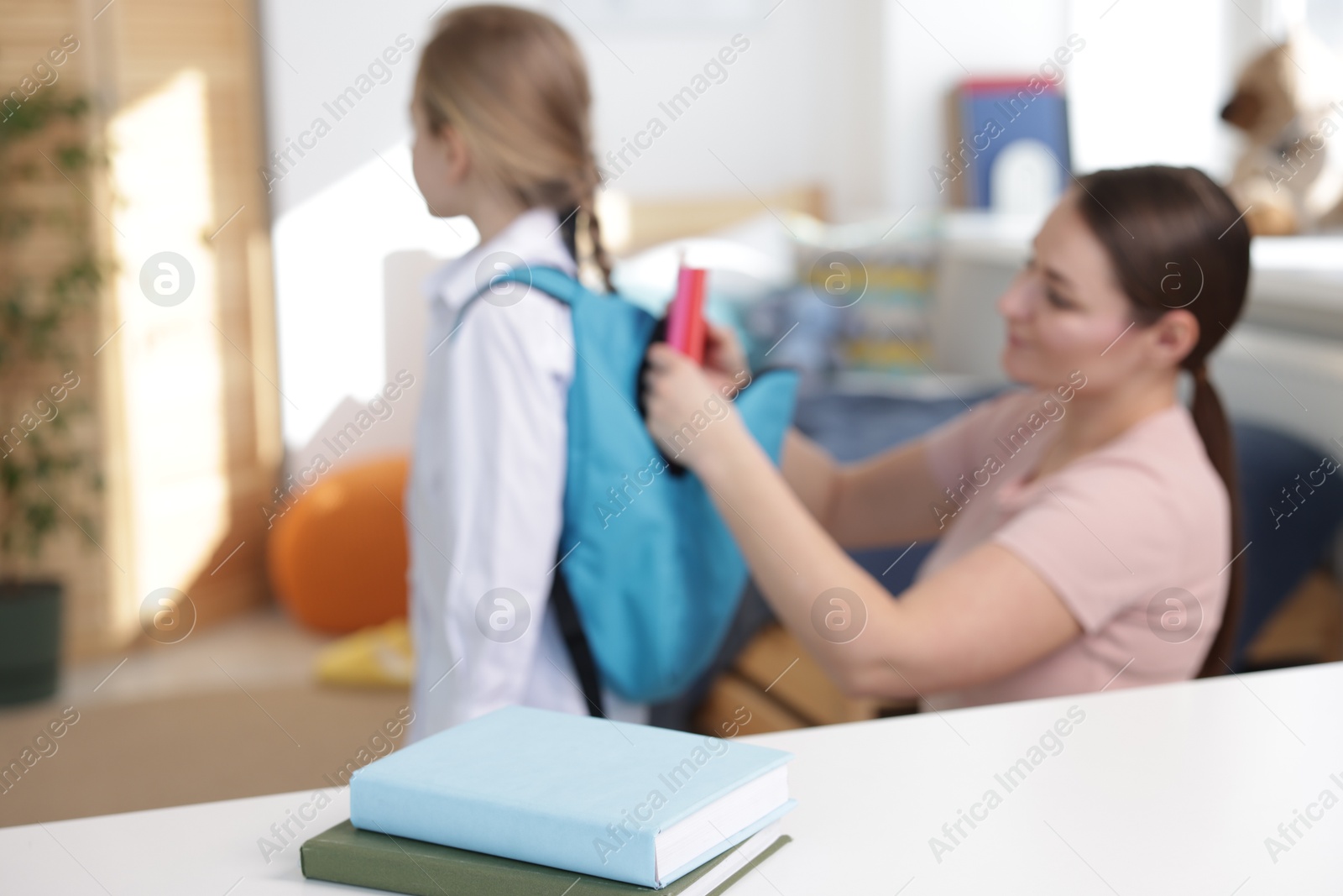 Photo of Mother helping her daughter packing backpack for school at home, focus on books