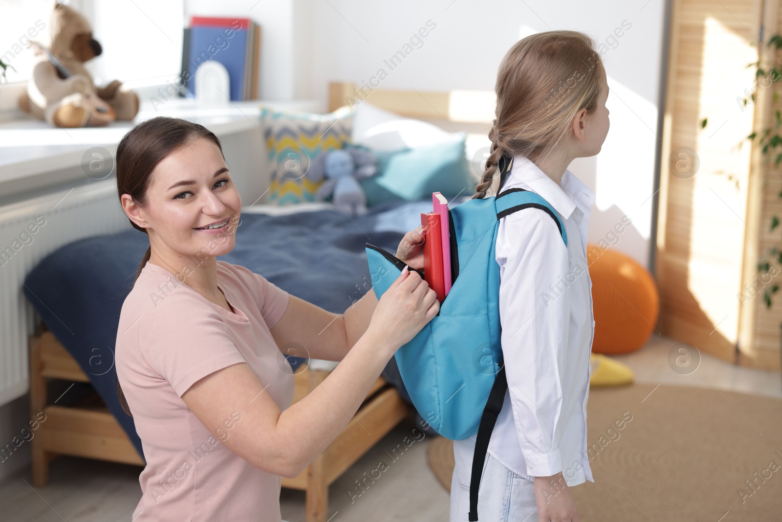 Photo of Mother helping her daughter packing backpack for school at home