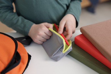 Photo of Boy packing pencil case at white table indoors, closeup