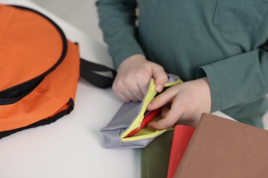 Photo of Boy packing pencil case at white table indoors, closeup