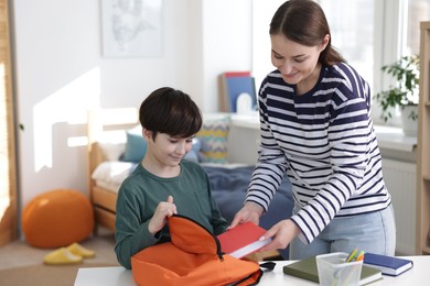 Mother helping her son packing backpack for school at home