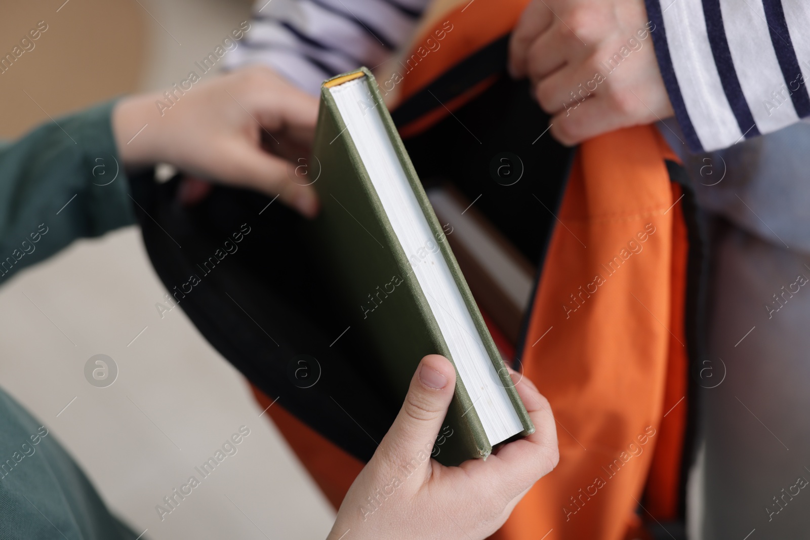 Photo of Mother helping her son packing backpack for school at home, closeup