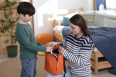 Mother helping her son packing backpack for school at home