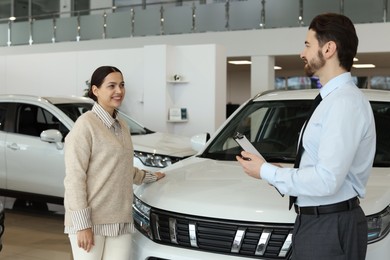 Photo of Happy salesman and client near new car in salon