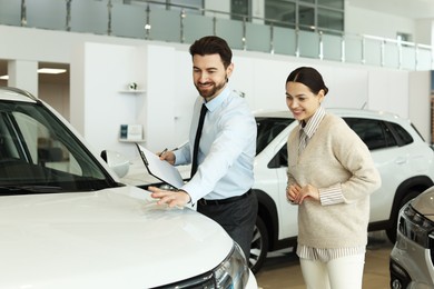 Photo of Happy salesman showing new car to client in salon