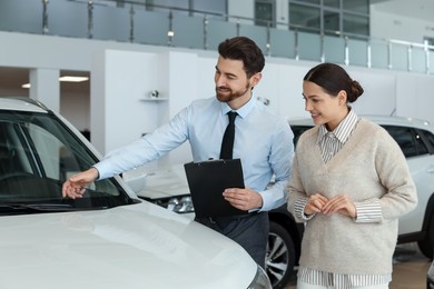 Photo of Happy salesman showing new car to client in salon