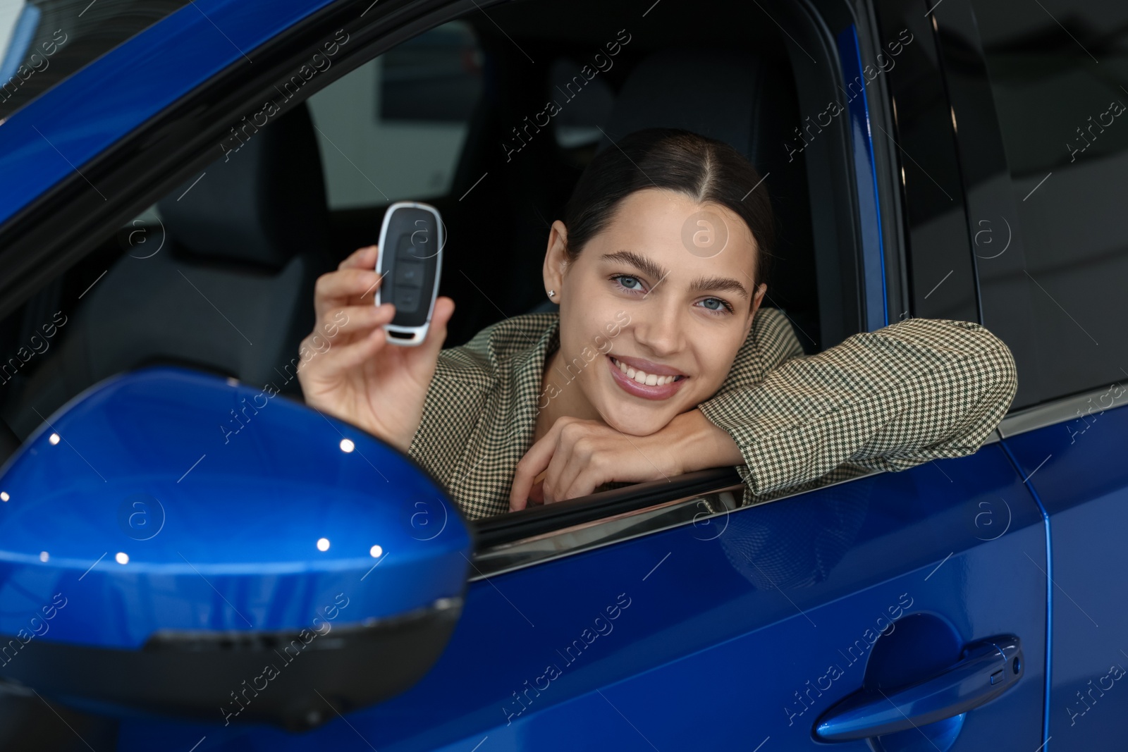 Photo of Happy woman with key inside new car in salon