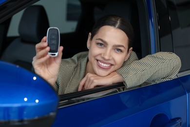 Photo of Happy woman with key inside new car in salon