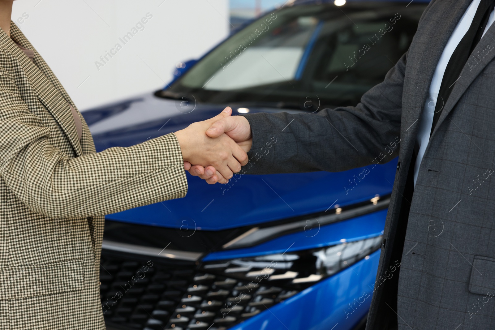 Photo of Saleswoman and client shaking hands near new car in salon, closeup