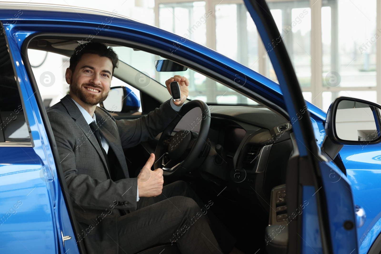 Photo of Happy man with key inside new blue car in salon