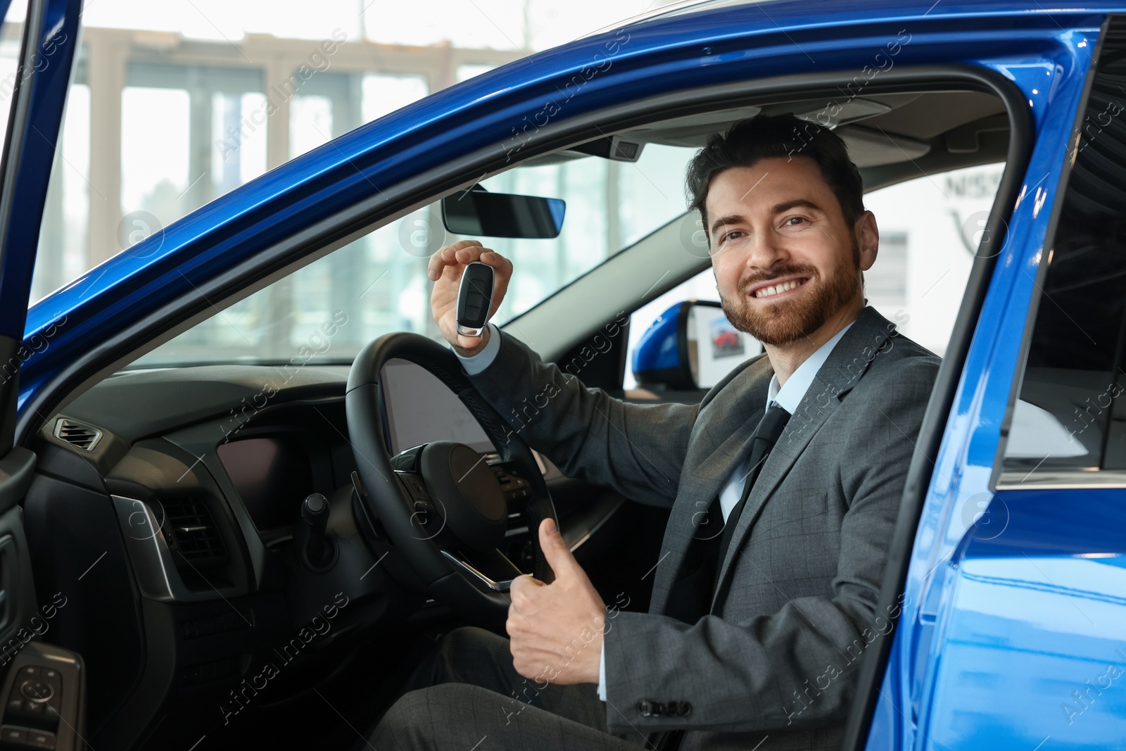 Photo of Happy man with key inside new blue car in salon