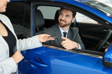 Photo of Saleswoman giving key to happy client inside new car in salon