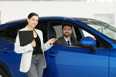 Happy saleswoman giving key to client inside new car in salon