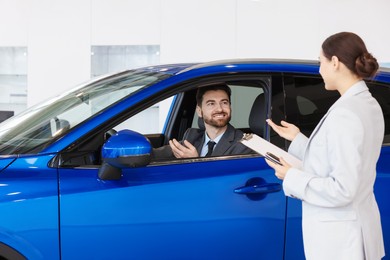 Happy saleswoman talking to client inside new car in salon