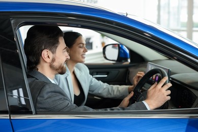 Happy saleswoman and client inside new car in salon, selective focus