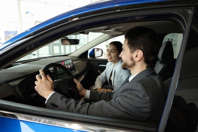 Happy saleswoman and client inside new car in salon, selective focus