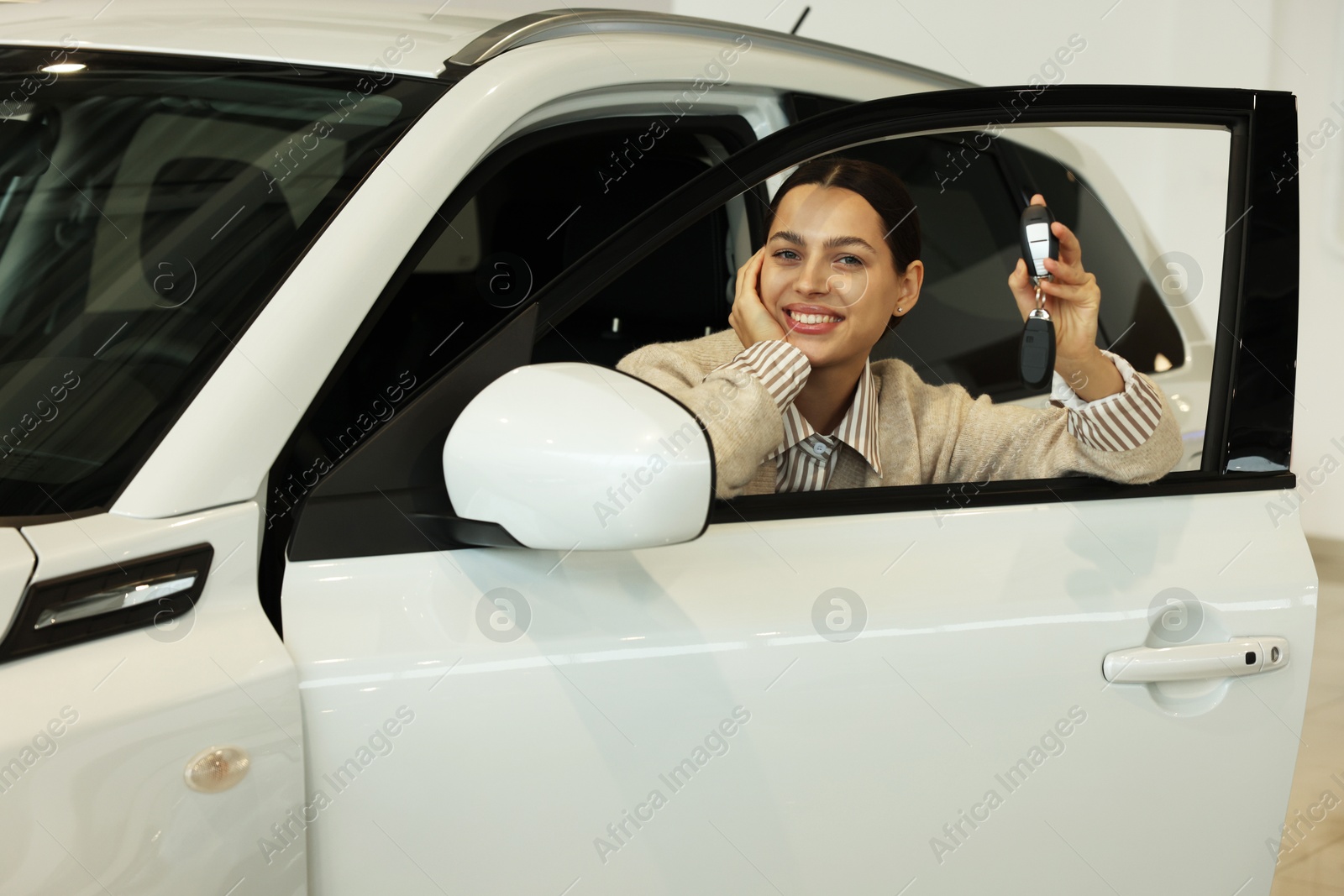 Photo of Happy woman with key inside new white car in salon