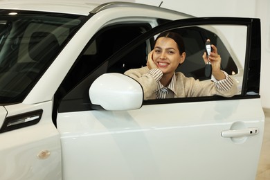 Happy woman with key inside new white car in salon