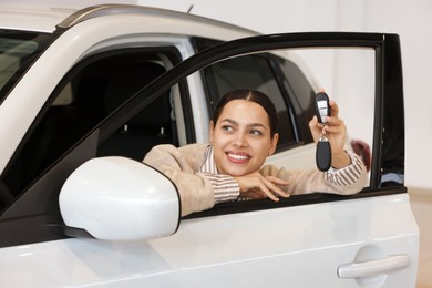 Happy woman with key inside new white car in salon