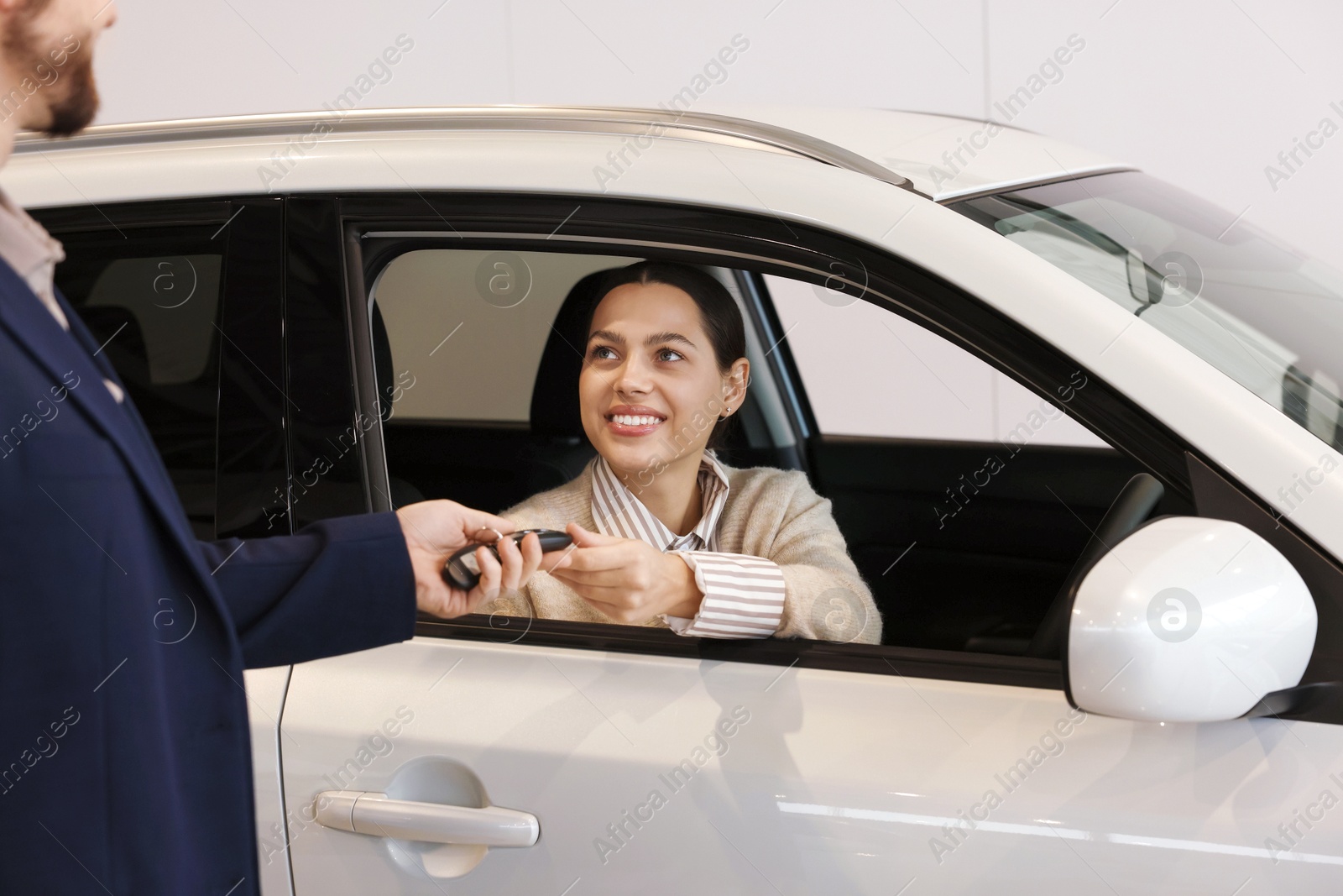 Photo of Salesman giving key to happy client inside new car in salon