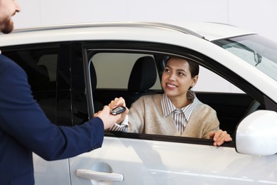 Photo of Salesman giving key to happy client inside new car in salon