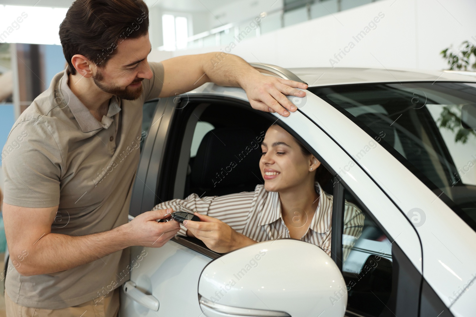 Photo of Happy husband giving key to his wife inside new car in salon