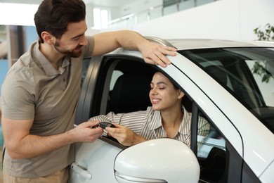 Happy husband giving key to his wife inside new car in salon