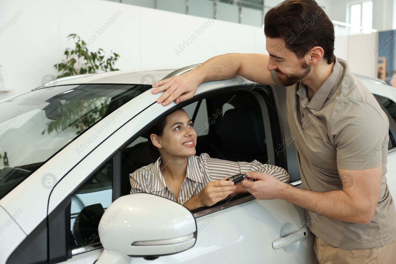 Photo of Happy husband giving key to his wife inside new car in salon