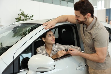 Happy husband giving key to his wife inside new car in salon