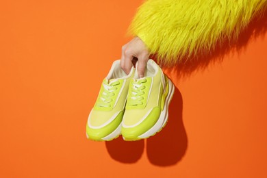 Photo of Woman showing stylish neon lime sneakers on orange background, closeup