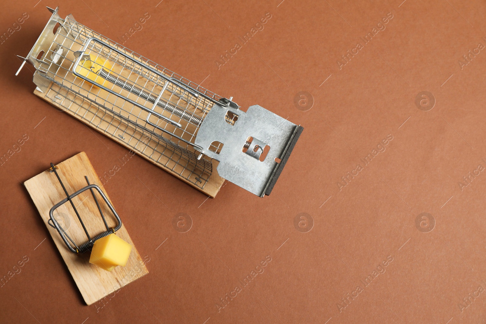 Photo of Two different mouse traps with bait on brown background, flat lay. Space for text