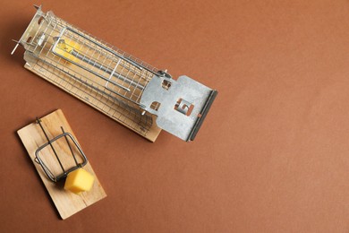 Two different mouse traps with bait on brown background, flat lay. Space for text