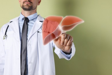 Doctor with stethoscope pointing at illustration of liver on olive color background, closeup