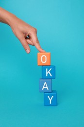 Image of Woman making word Okay with colorful cubes on light blue background, closeup