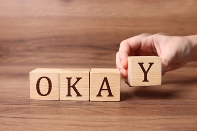 Image of Woman making word Okay with cubes on wooden background, closeup