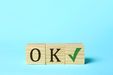 Wooden cubes with abbreviation OK and check mark on light blue background