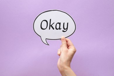 Image of Woman holding paper speech bubble with word Okay on lilac background, closeup