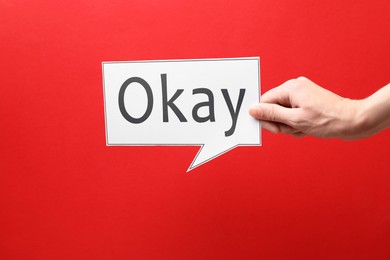 Image of Woman holding paper speech bubble with word Okay on red background, closeup