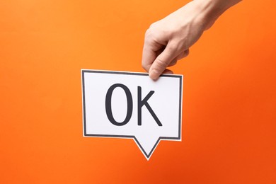 Image of Woman holding paper speech bubble with abbreviation OK on orange background, closeup