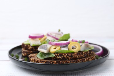 Tasty sandwiches with herring, onions, lettuce and olives on white table, closeup