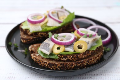 Tasty sandwiches with herring, onions, lettuce and olives on white wooden table, closeup