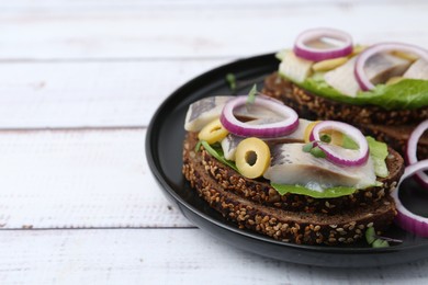 Photo of Tasty sandwiches with herring, onions, lettuce and olives on white wooden table, closeup. Space for text