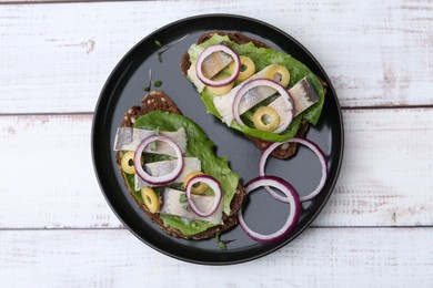 Photo of Tasty sandwiches with herring, onions, lettuce and olives on white wooden table, top view