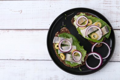 Photo of Tasty sandwiches with herring, onions, lettuce and olives on white wooden table, top view. Space for text