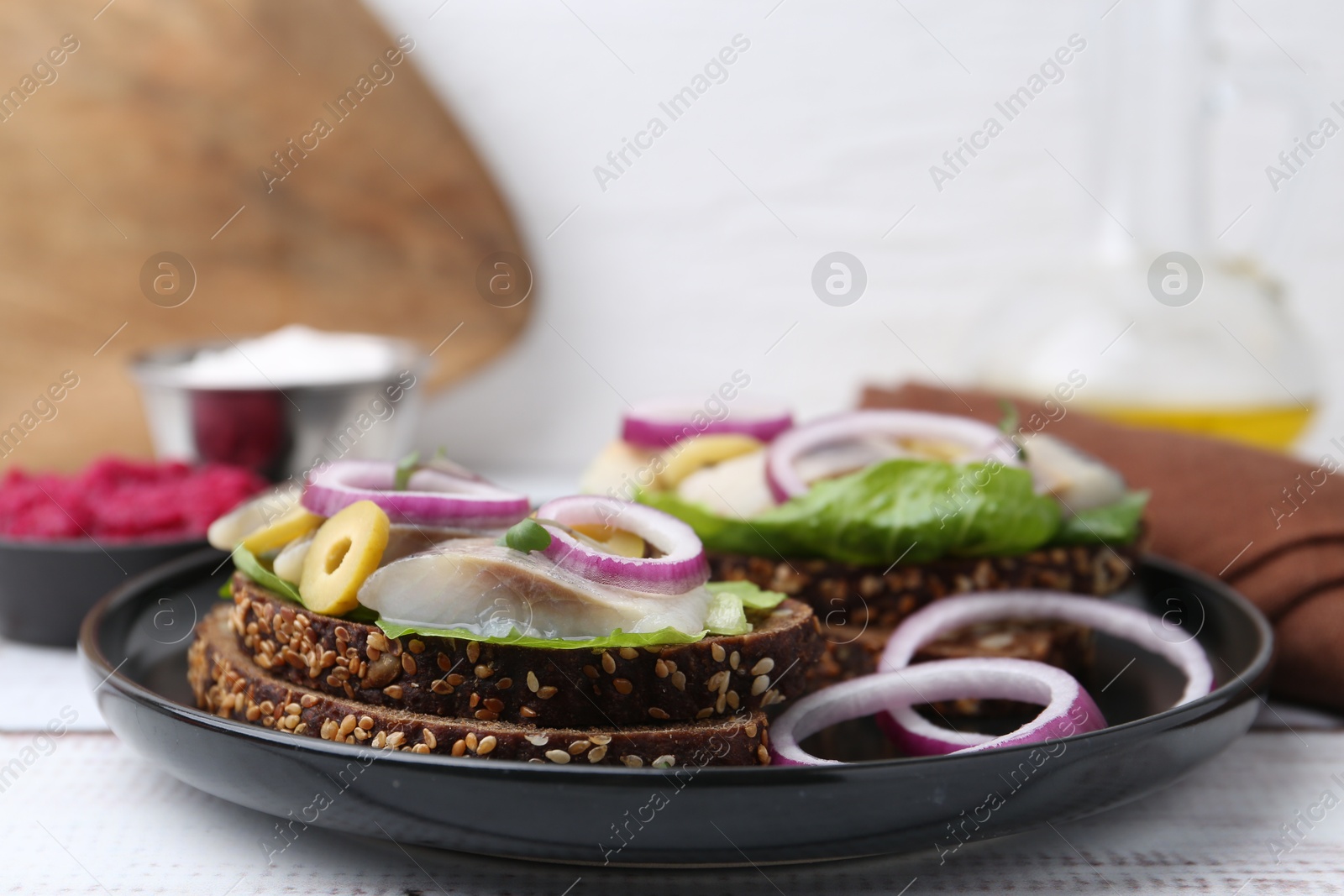 Photo of Tasty sandwiches with herring, onions, lettuce and olives on white wooden table, closeup